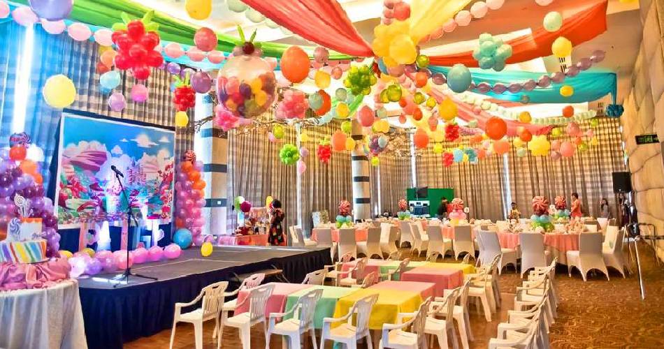 A party hall decorated with colorful balloons and fabrics. Stage set up with scenary background.